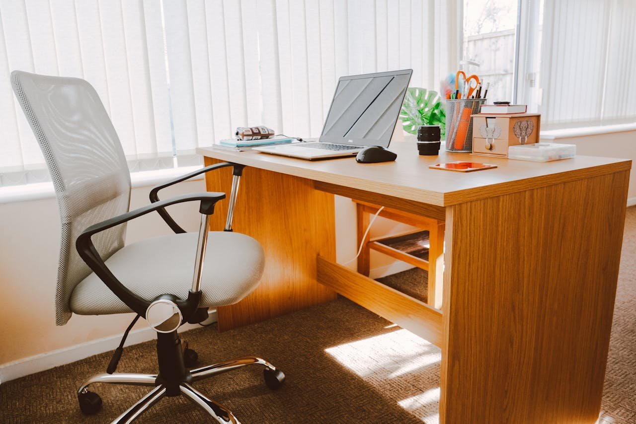 about-img A modern office workspace featuring a wooden desk, chair, laptop, and bright natural light.